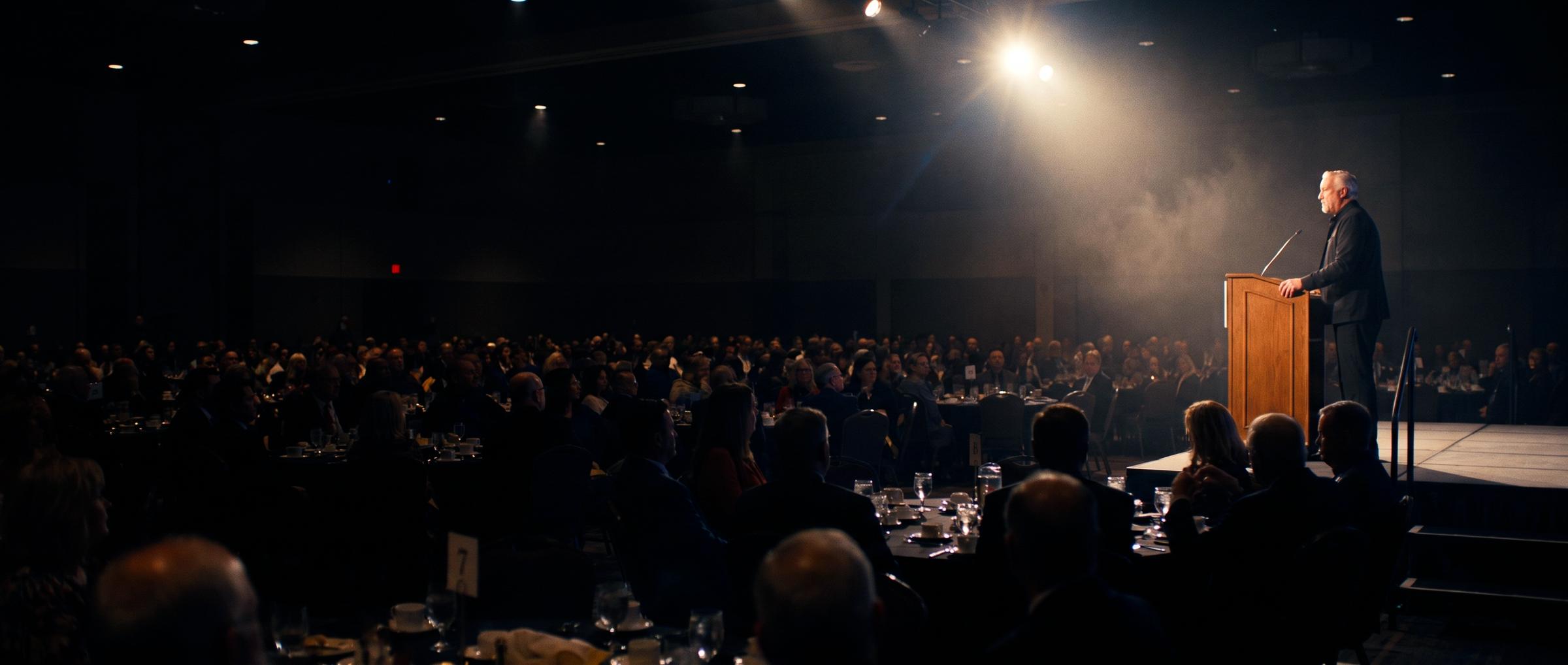 Fr. Dan Reehil speaking from a podium to a full banquet hall